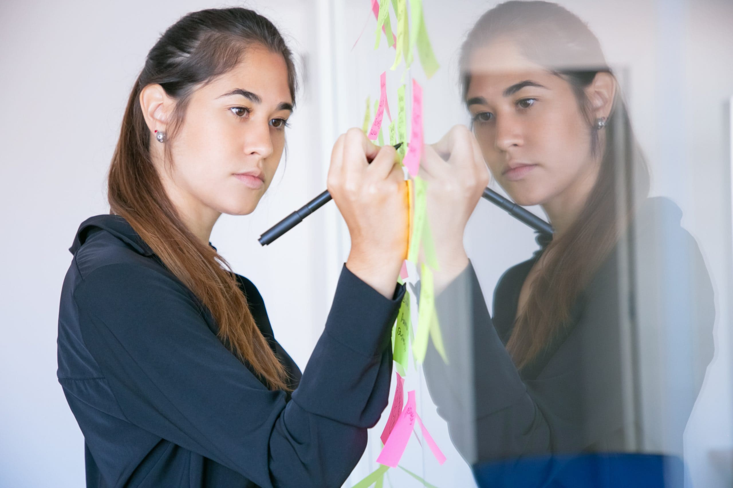 beautiful-young-latin-businesswoman-writing-sticker-with-marker-concentrated-professional-female-manager-sharing-idea-project-making-note-scaled-1-1